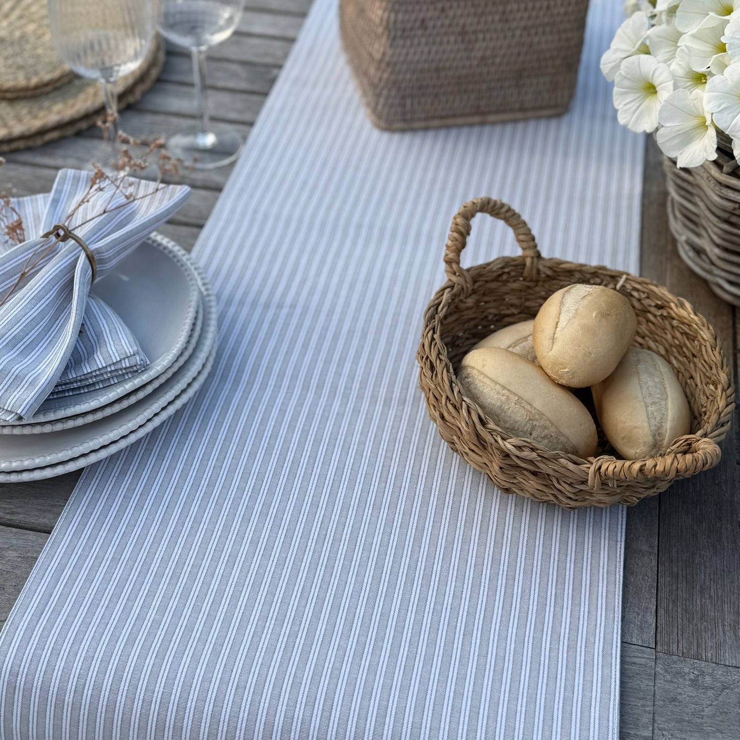 Table setting with a basket of bread on a striped grey and white table runner.