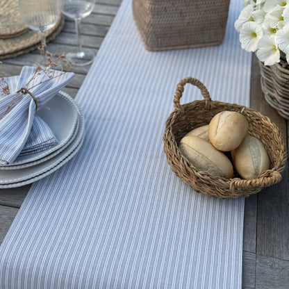 Table setting with a basket of bread on a striped grey and white table runner.