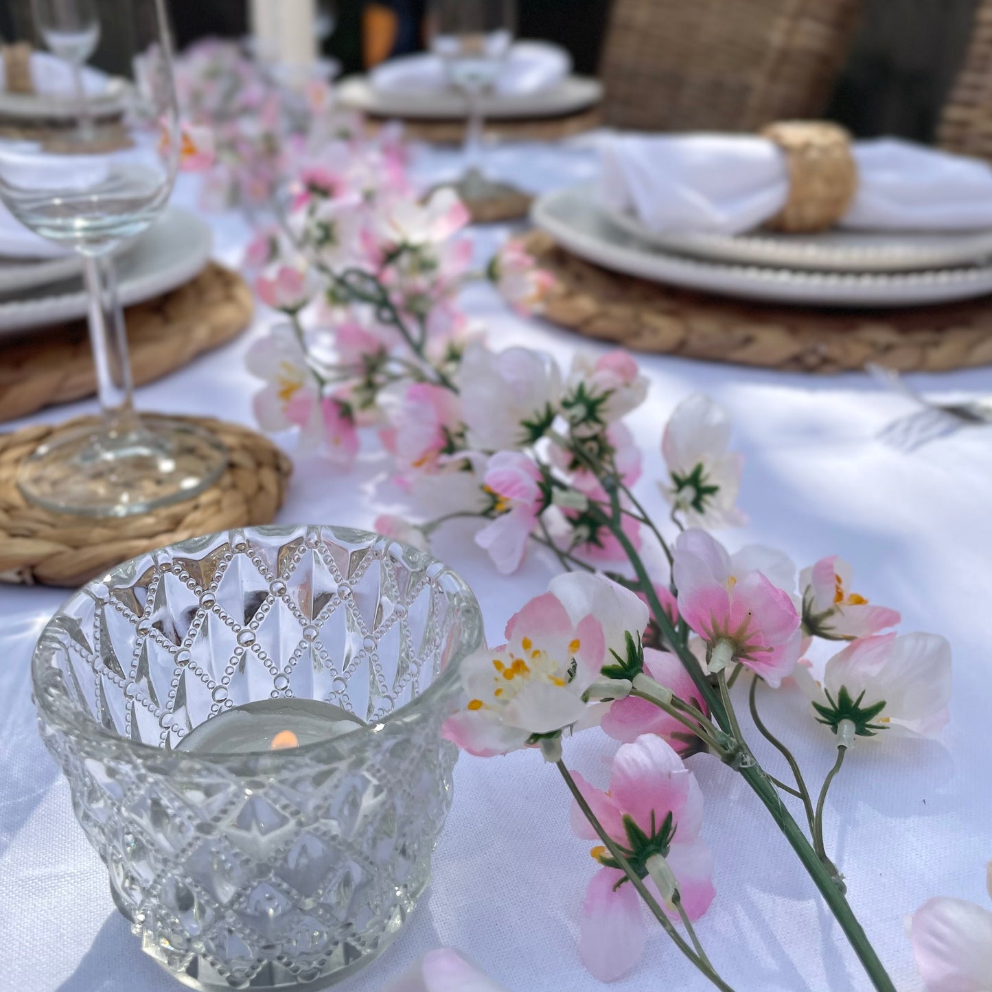 Pink cherry blossom garland with delicate lifelike petals and hanging loops. Styled on a garden dining table.