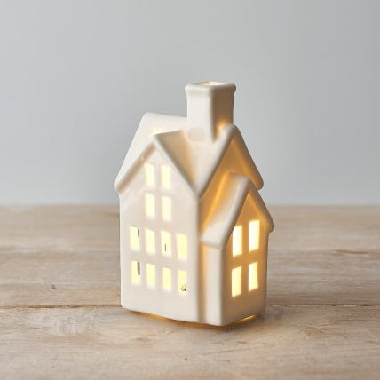 Small white glazed ceramic LED house ornament with warm light, styled on a wooden mantel.