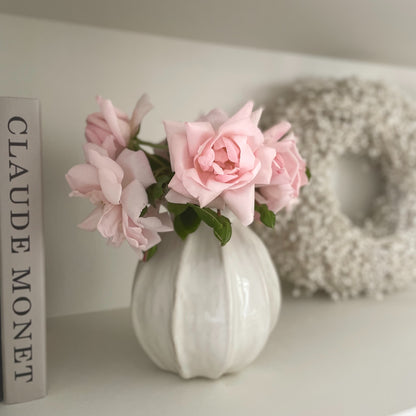 Off white ceramic poppy vase styled with a pink rose on a neutral side table.