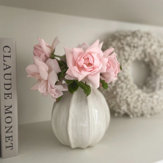 Off white ceramic poppy vase styled with a pink rose on a neutral side table.