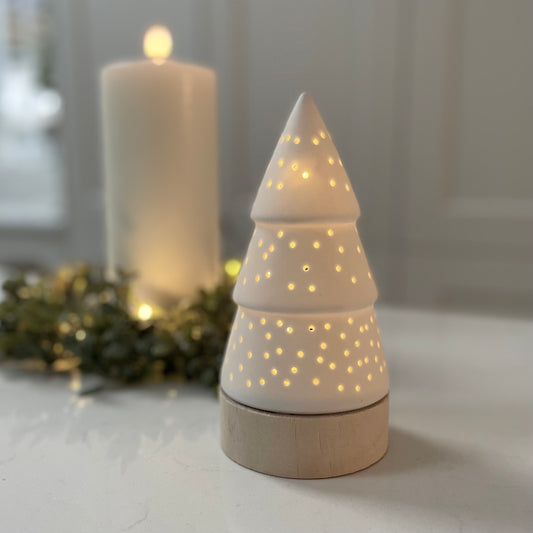 White matte light up tree decoration with cut out design glowing softly on table. 17 cm.