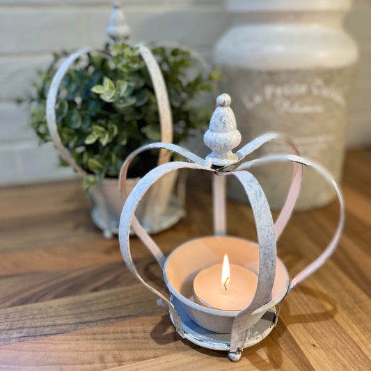 Decorative candle holder shaped like a crown with a lit candle on a wooden surface.