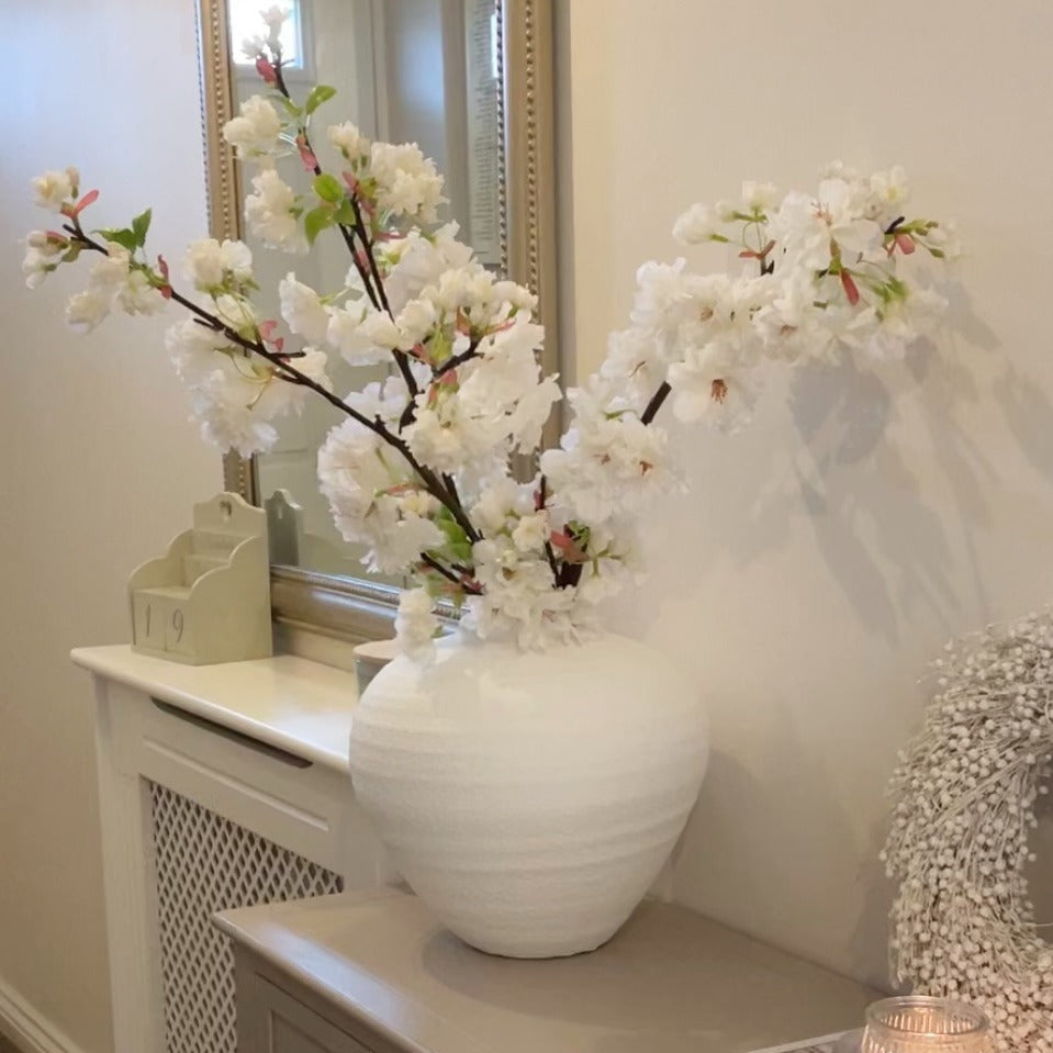 White vase with apple blossom branches styled on a beige console in a hallway.