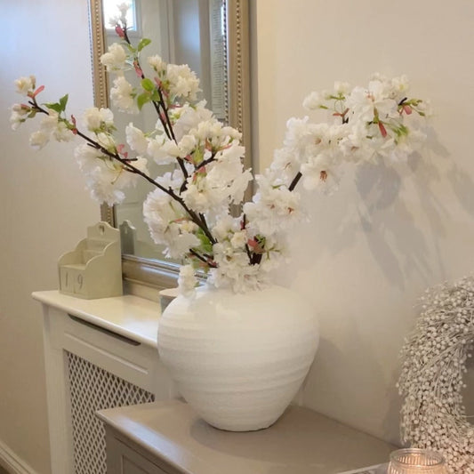 White vase with apple blossom branches styled on a beige console in a hallway.