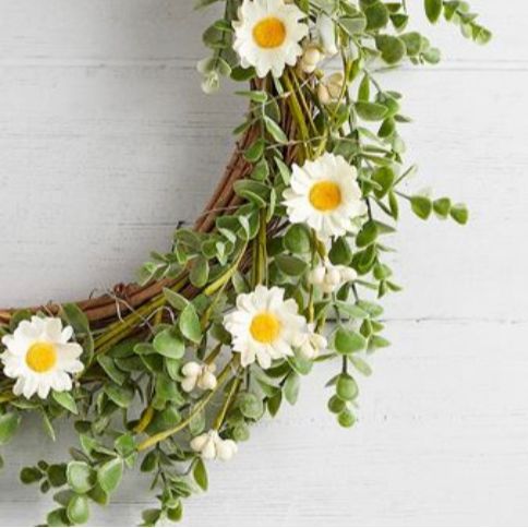 Close up of white daisies on greenery wreath, styled on a white wooden rustic wall.