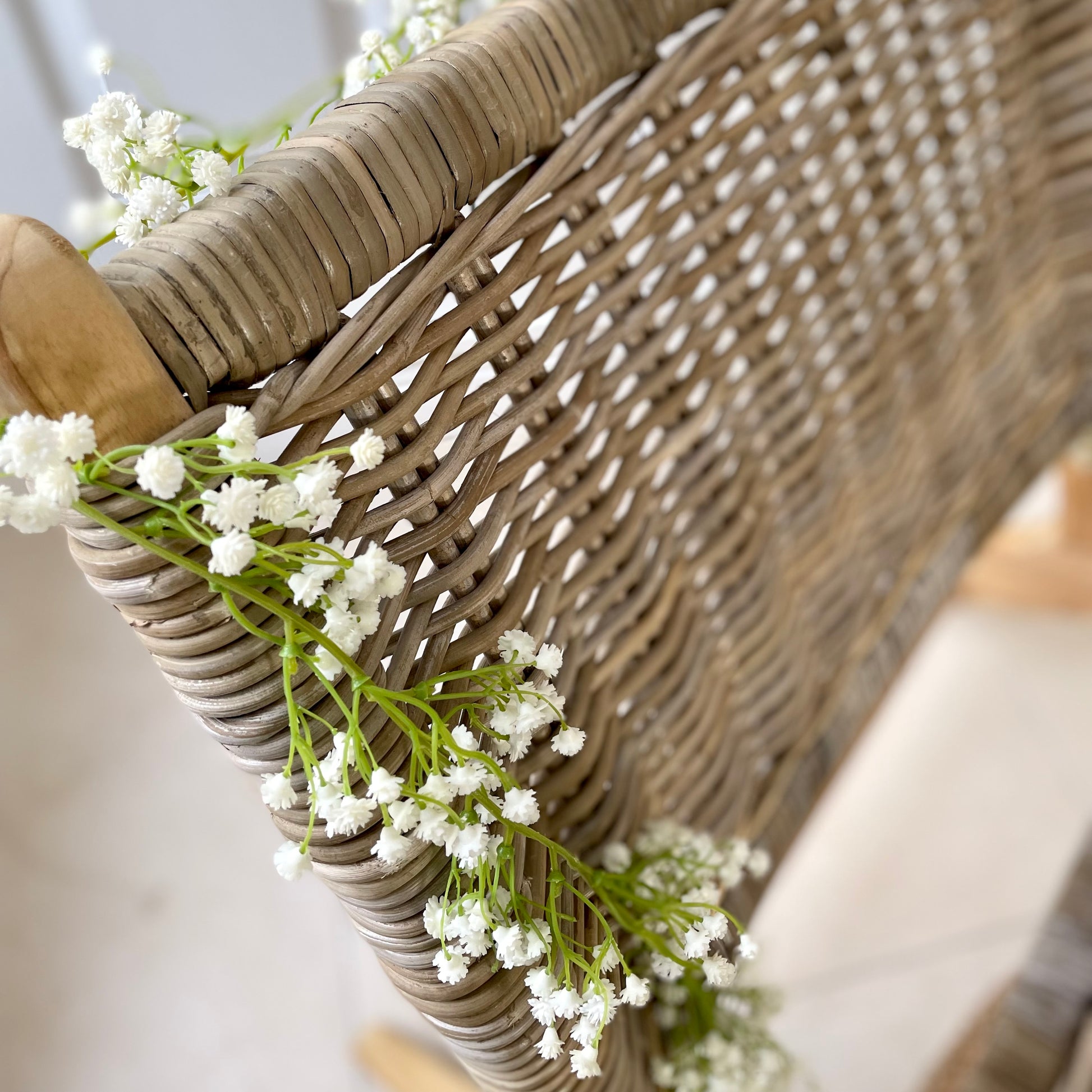 White faux gypsophila flower garland draped on a rattan chair.