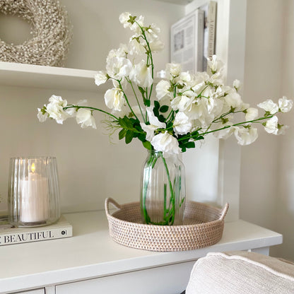 White faux sweet pea stems styled in a glass vase on a wooden table for a soft, elegant look.