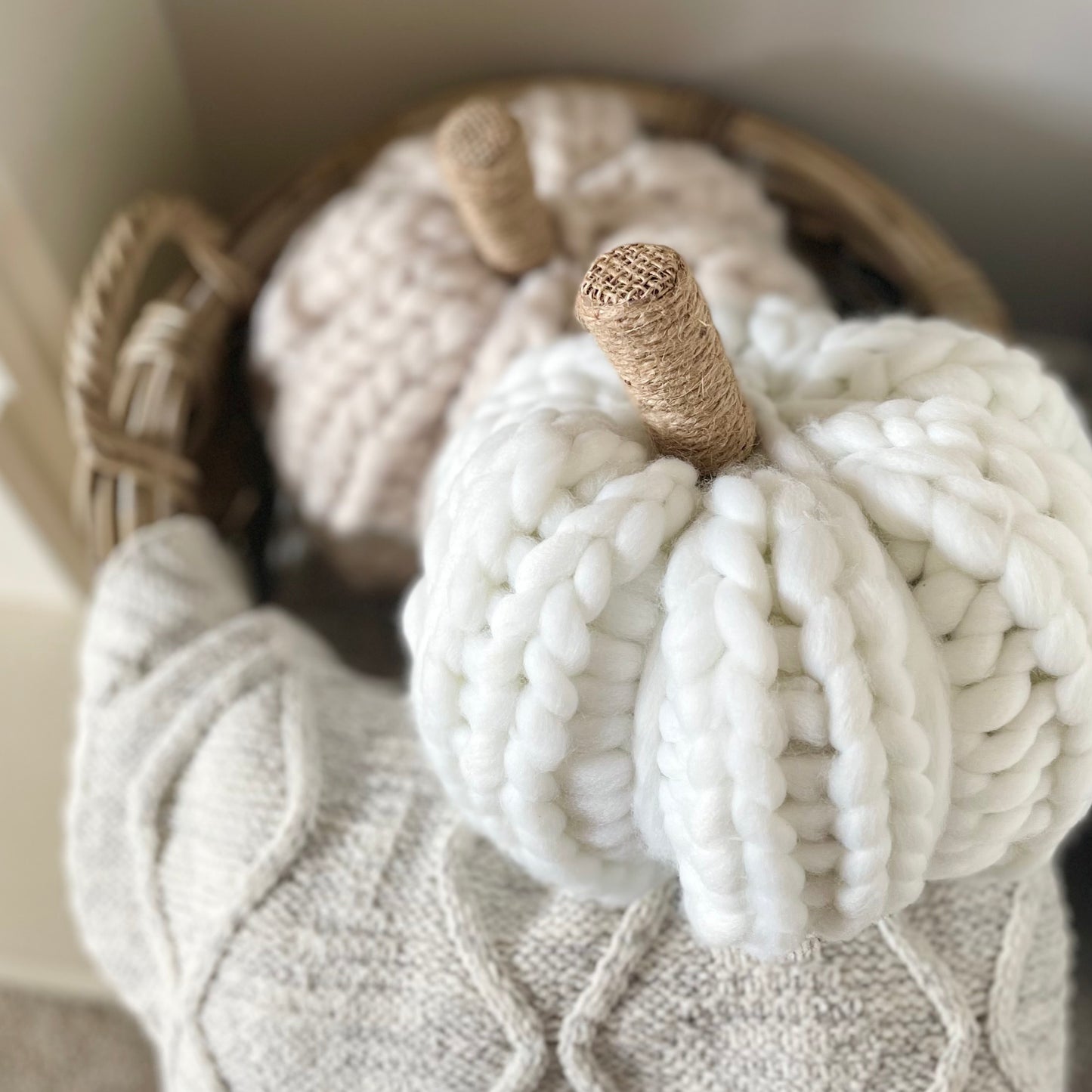 White chunky knitted pumpkin with twine stalk styled next to a rustic basket with cable knit throw.