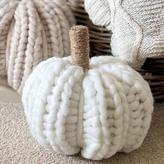 White chunky knitted pumpkin with twine stalk styled next to a rustic basket with cable knit throw.