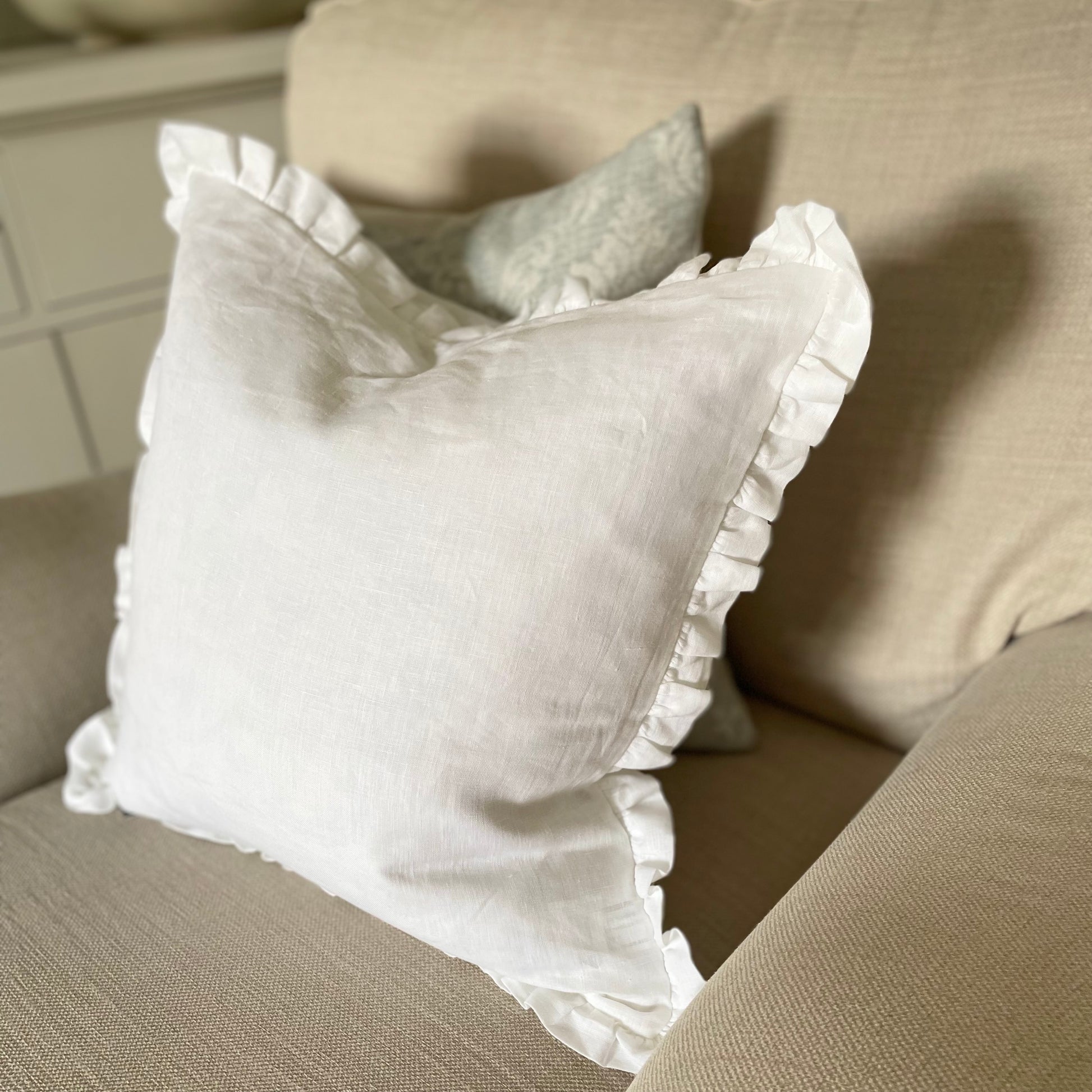 White linen cushion with ruffled edge and mother of pearl button detail styled on a chair with textured blue cushion.