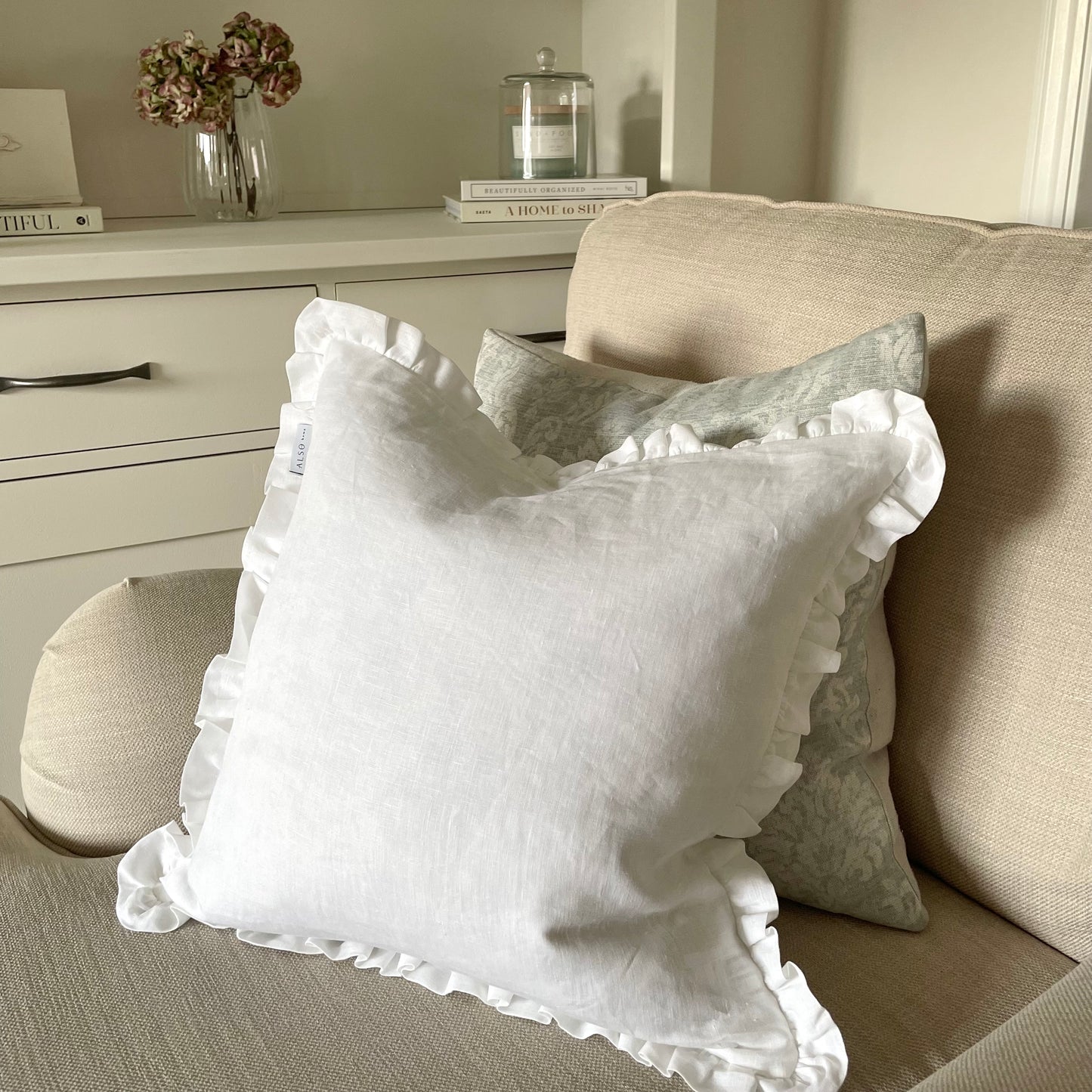 White linen cushion with ruffled edge and mother of pearl button detail styled on a chair with a green textured cushion.