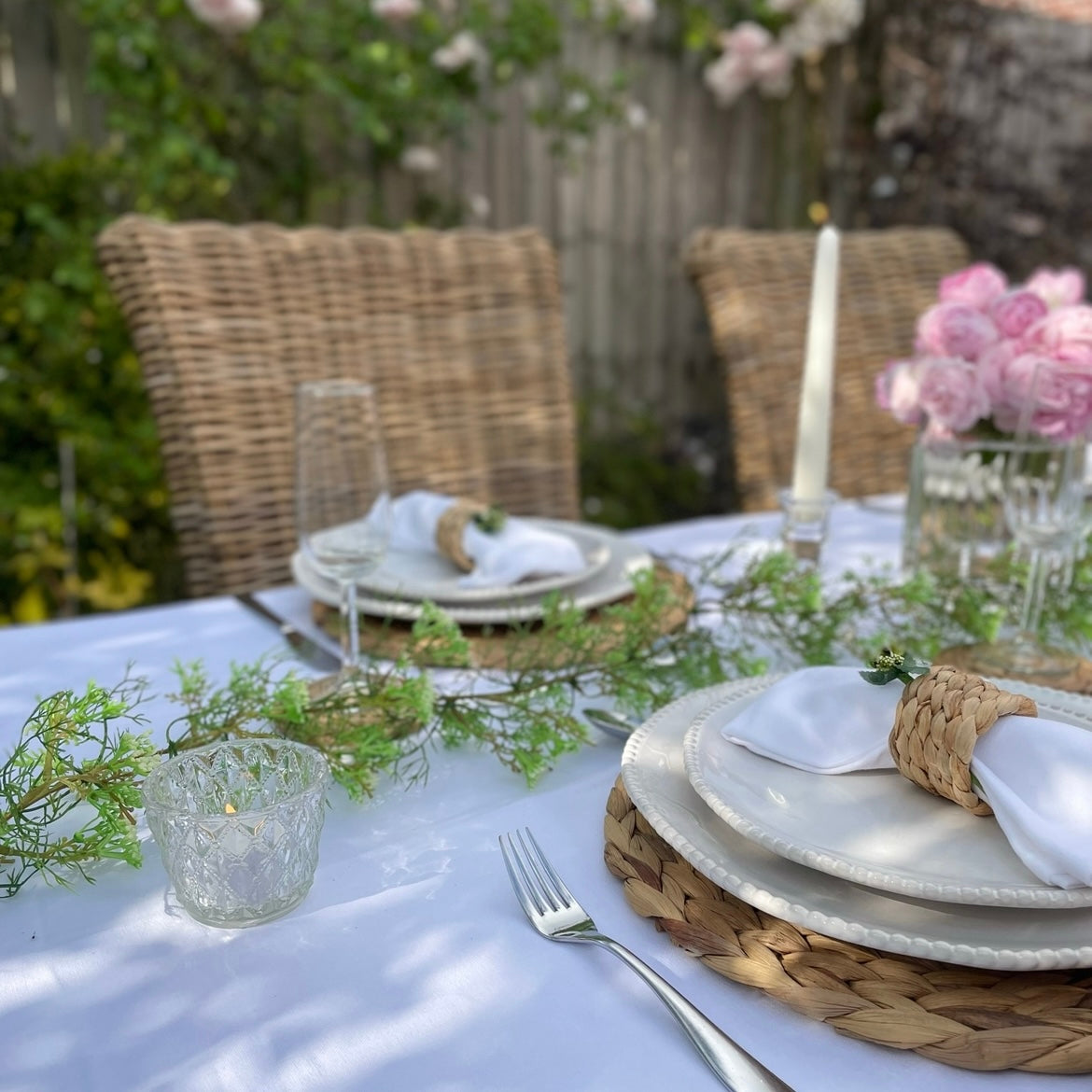 Classic eco friendly 100% white linen table cover styled for dinner in a garden dining table. Shown with roses and candles.