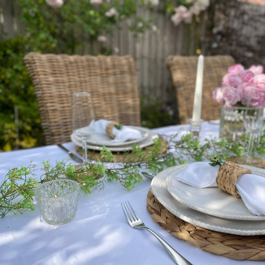 Classic eco friendly 100% white linen table cover styled for dinner in a garden dining table. Shown with roses and candles.