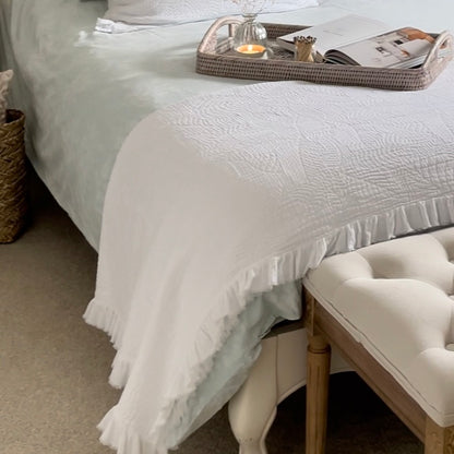 White quilted bedspread with embroidered texture and frilled edges.Styled in a cosy neutral bedroom.