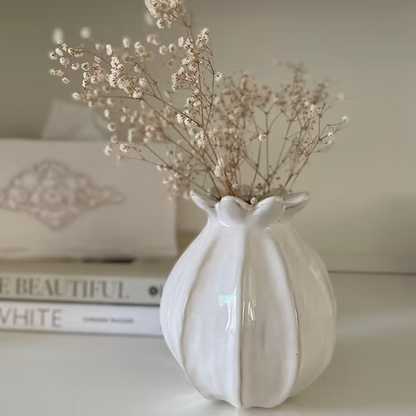 White ceramic vase with dried flowers on a surface with books in the background.