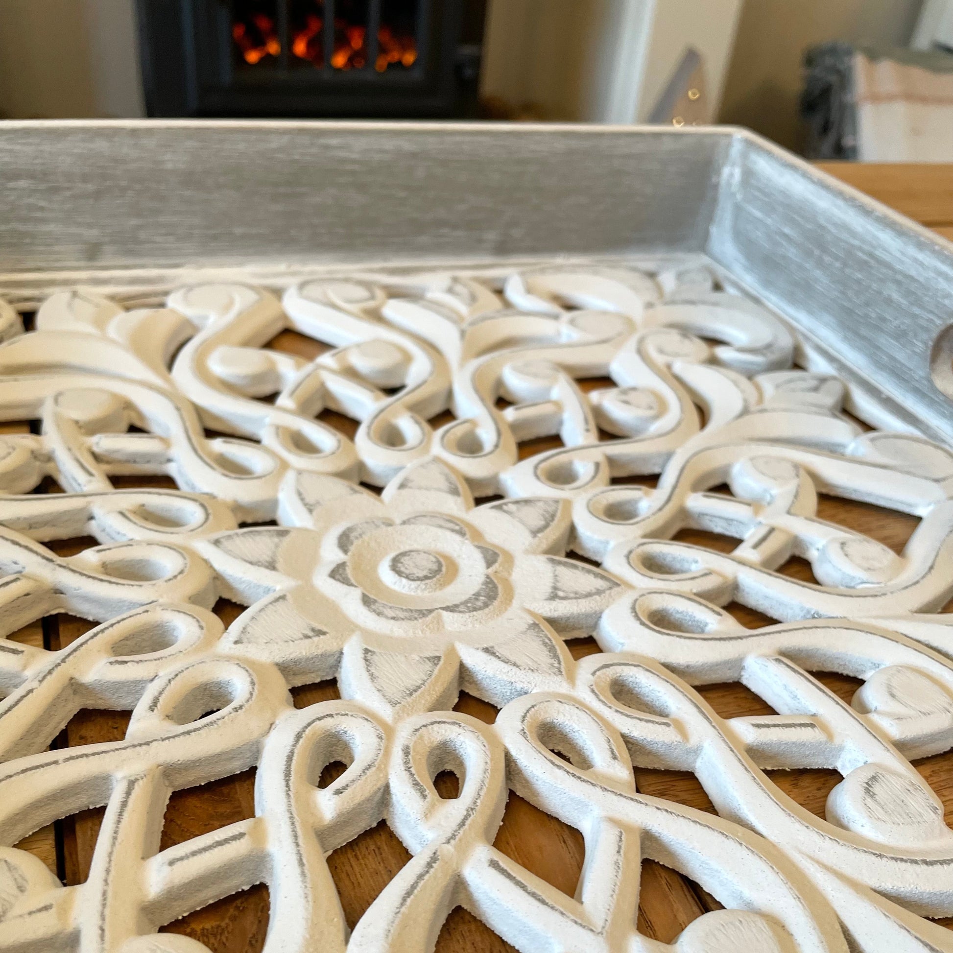 Whitewashed carved wooden tray with distressed finish and side handles, styled with candles and neutral decor on a wooden table.