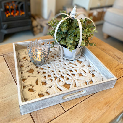 Whitewashed carved wooden tray with distressed finish and side handles, styled with candles and neutral decor on a wooden table.