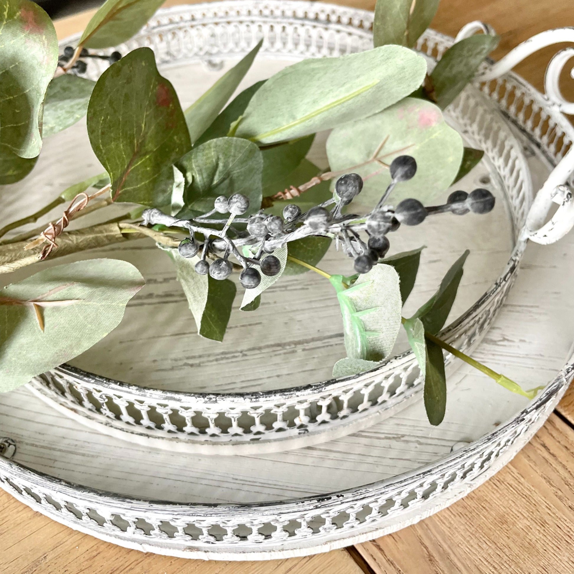 White washed decorative trays with greenery on a wooden surface.