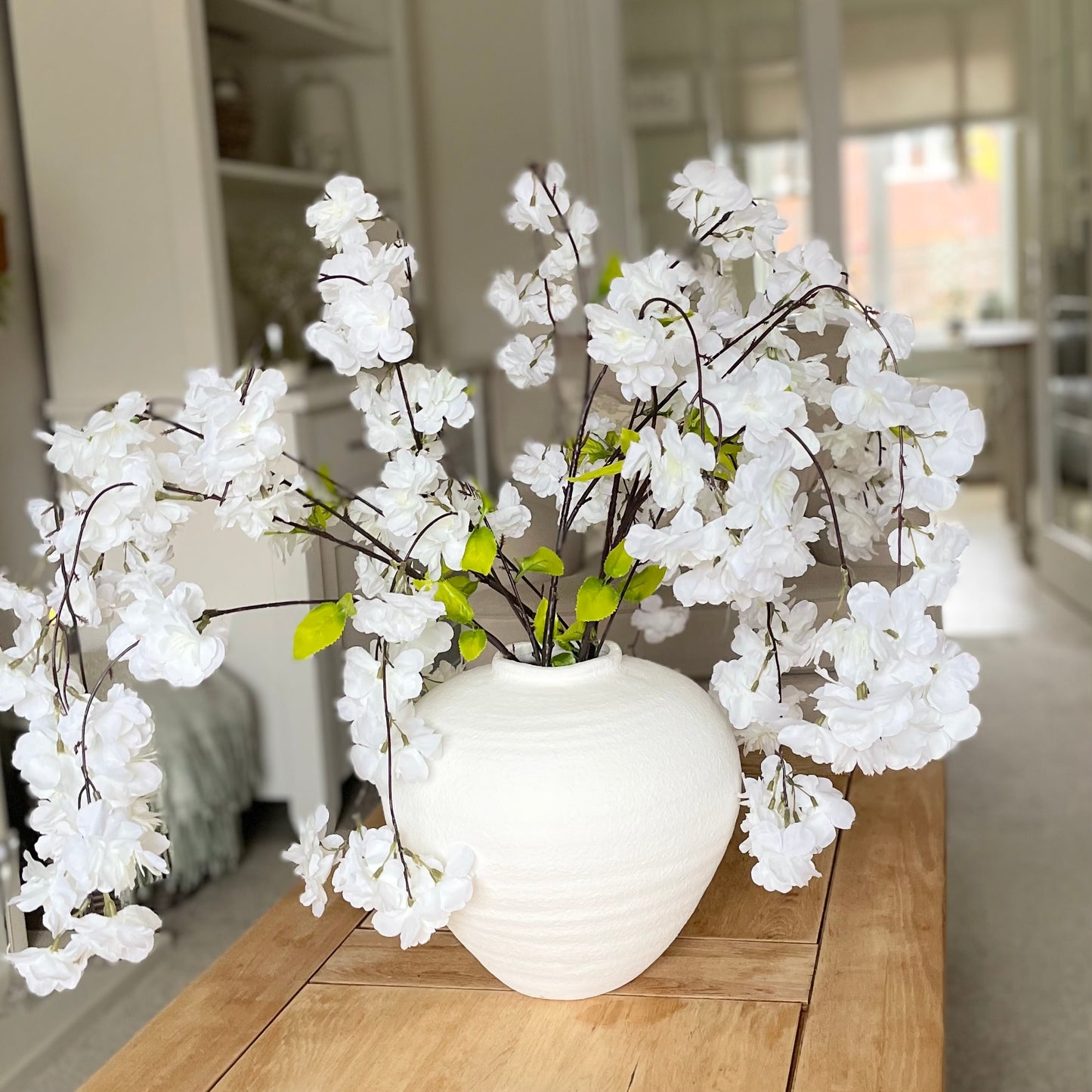 Lifelike white weeping cherry blossom stem styled in a vase on a coffee table.