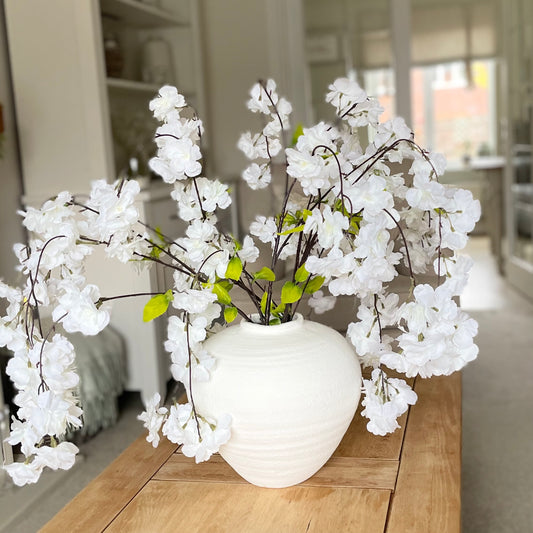 Lifelike white weeping cherry blossom stem styled in a vase on a coffee table.