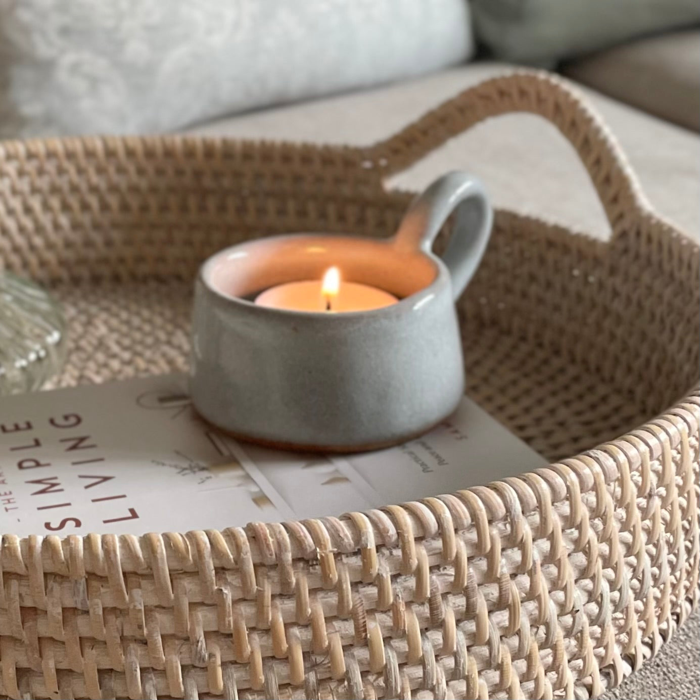 Whitewashed round rattan tray with handles styled on a coffee table with home accessories.