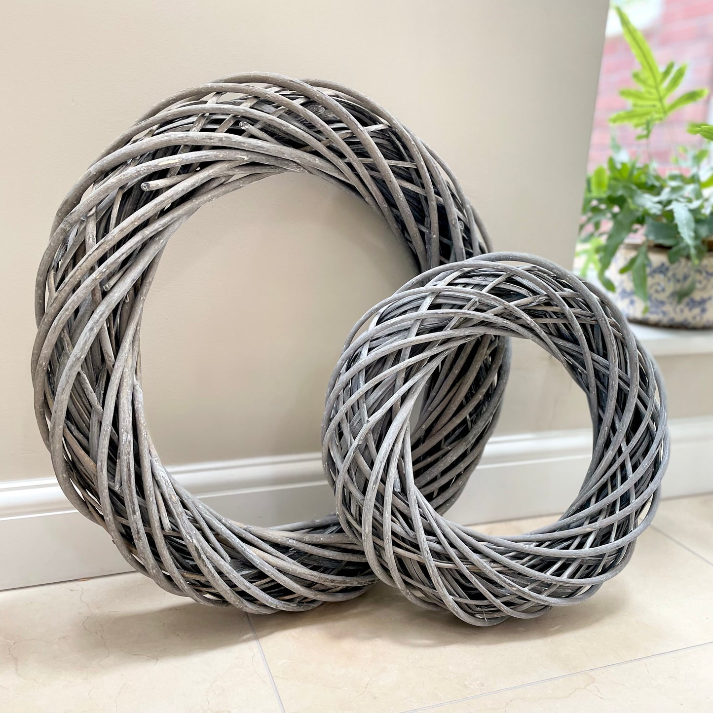 Grey white washed rattan wreaths with entwined design. Small and large, styled on a neutral wall.