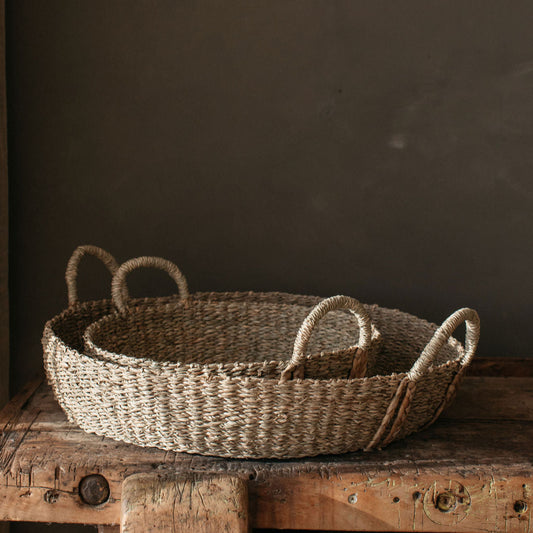 Handwoven natural seagrass basket with plaited handles, styled on a coffee table with books and candles for a warm, rustic look.