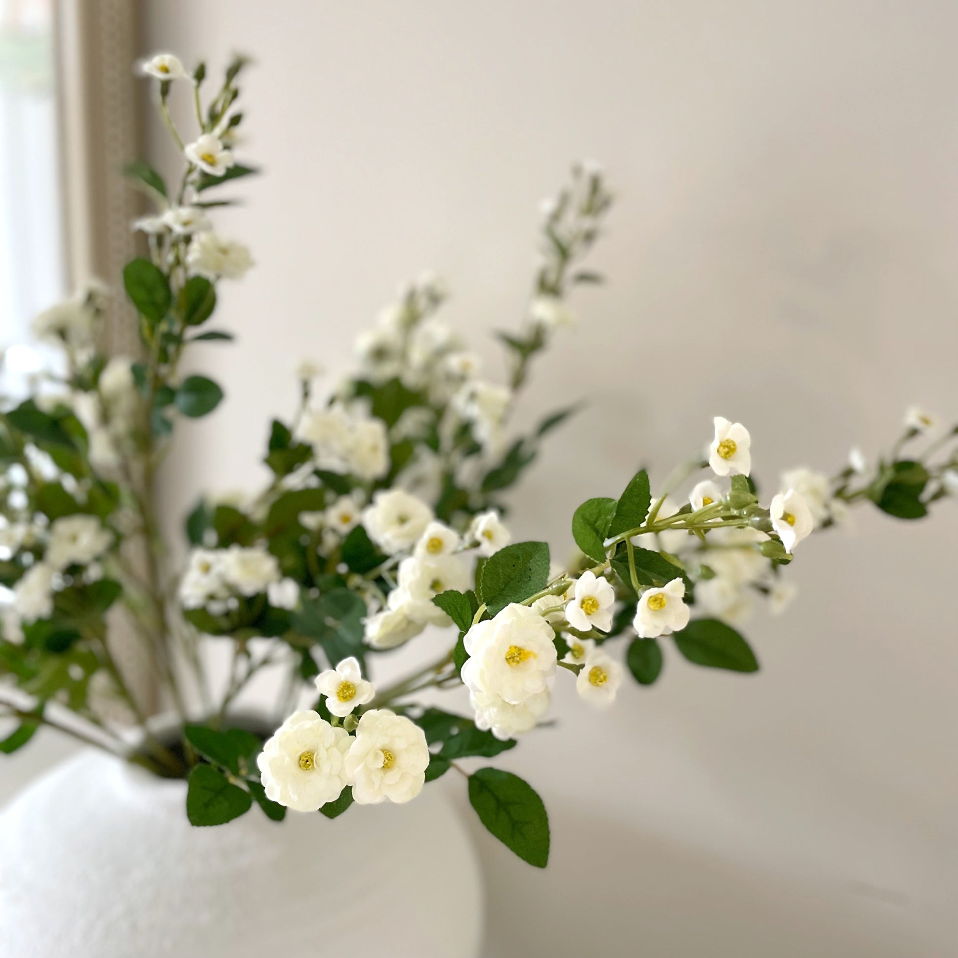 Wild Meadow White Rose Stem with delicate white flowers, soft yellow centres, and realistic green leaves, styled in a vase for timeless home decor.