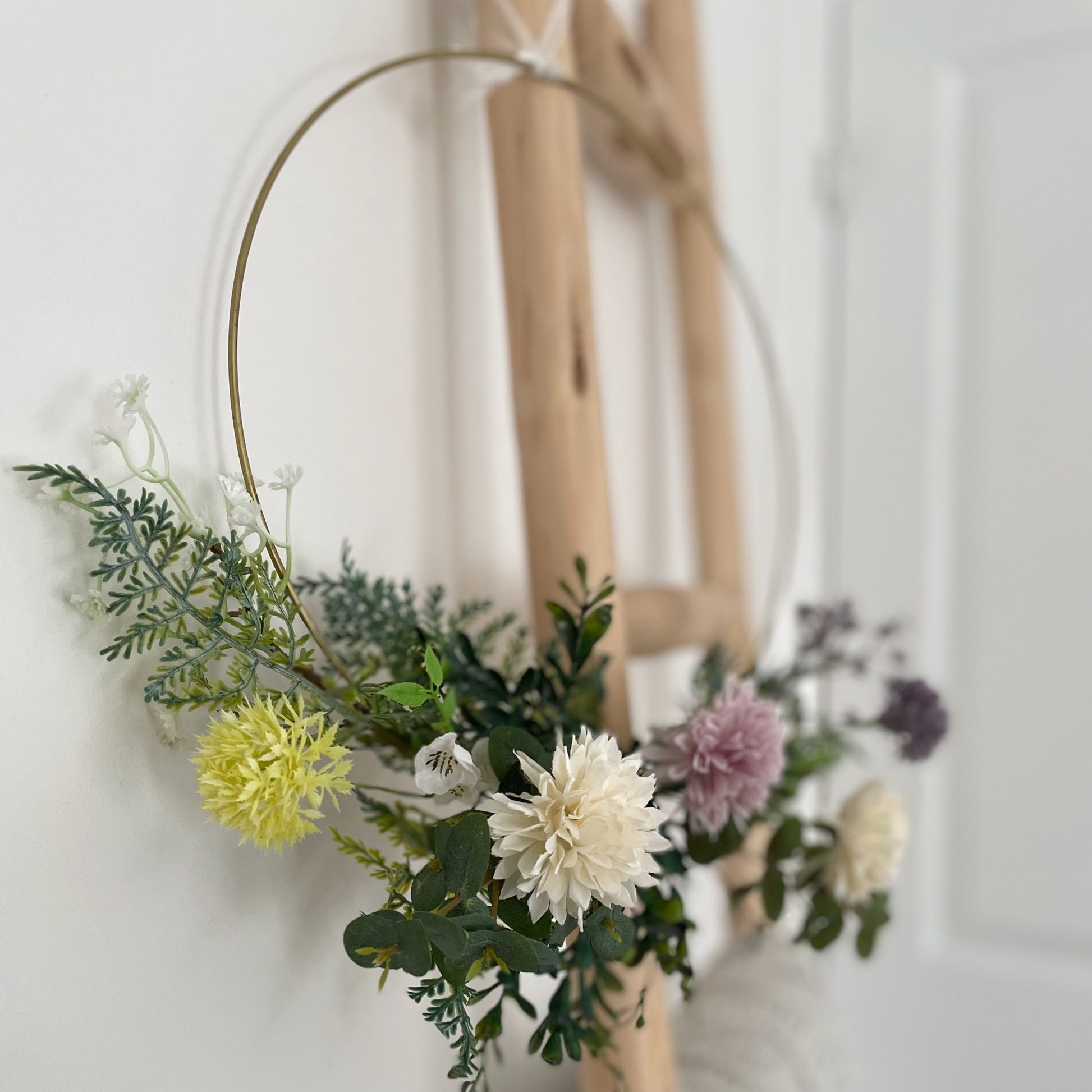 Whimsical hoop wreath decorated with artificial wild flowers and green foliage hanging on a rustic ladder.