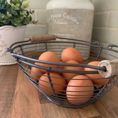Wire basket with wooden handles holding eggs, styled on a neutral kitchen countertop.