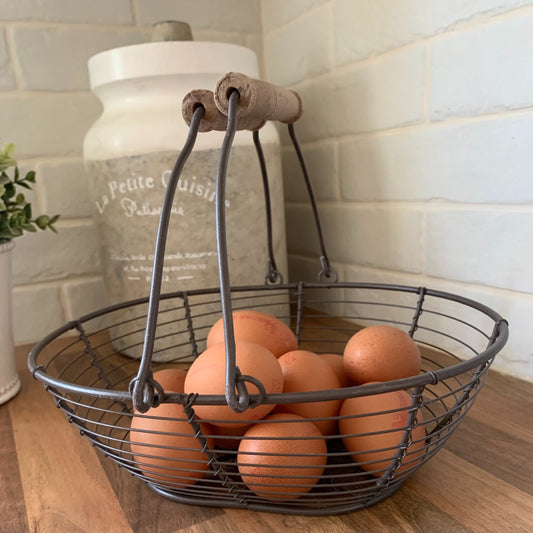 Wire basket with wooden handles holding eggs, styled on a neutral kitchen countertop.