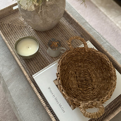 Woven basket with handles on a surface next to a candle and decorative items.