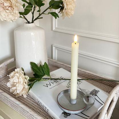 Grey washed zinc wee willie winkie candle holder styled with a taper candle on a rattan tray on a bedside cabinet.