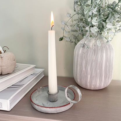 Grey washed wee willie winkie zinc candle holder styled with a taper candle on a wooden console table, with books and a vase of foliage.